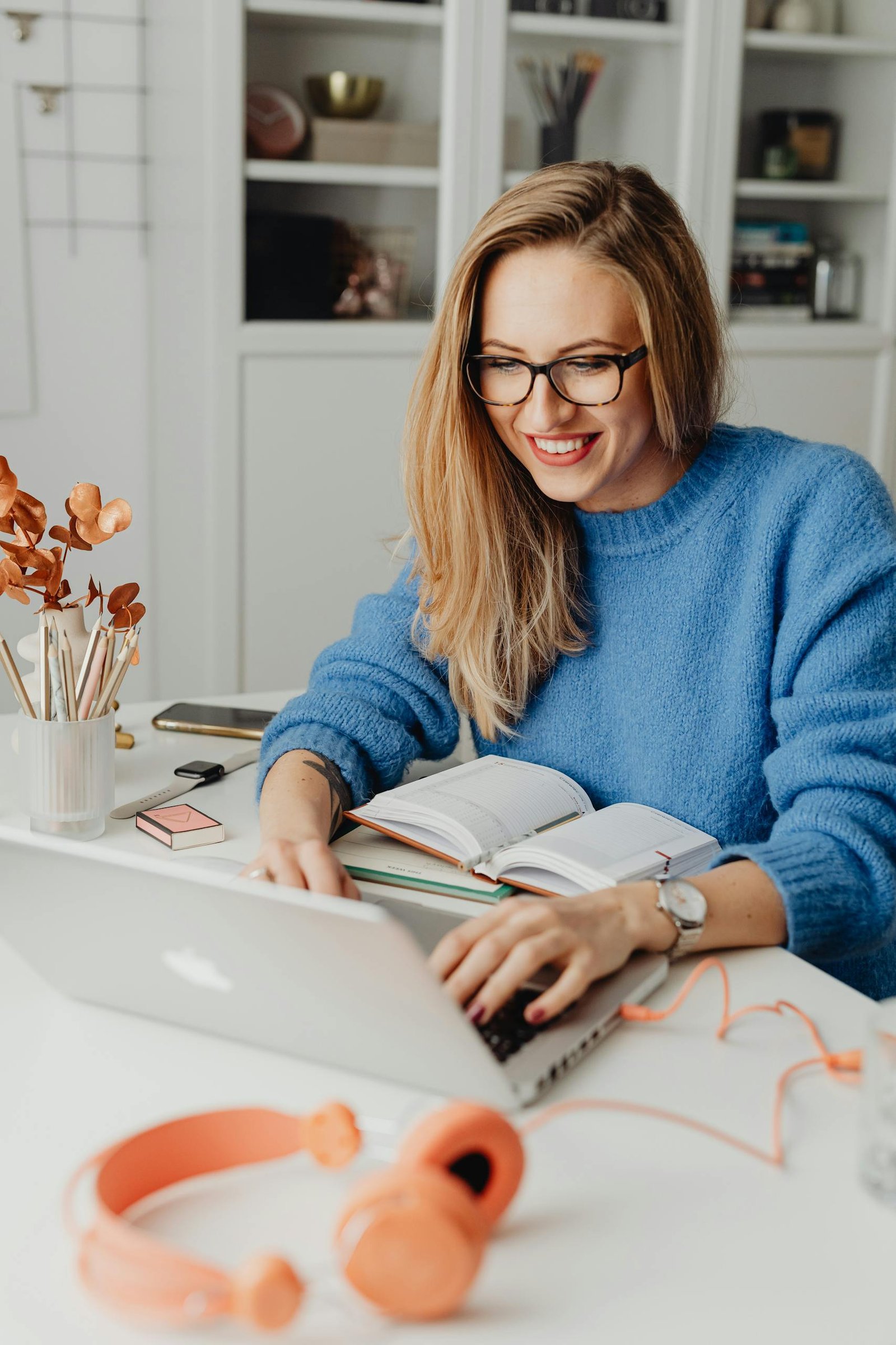 A cheerful woman in a blue sweater working remotely with a laptop in a cozy home setting.