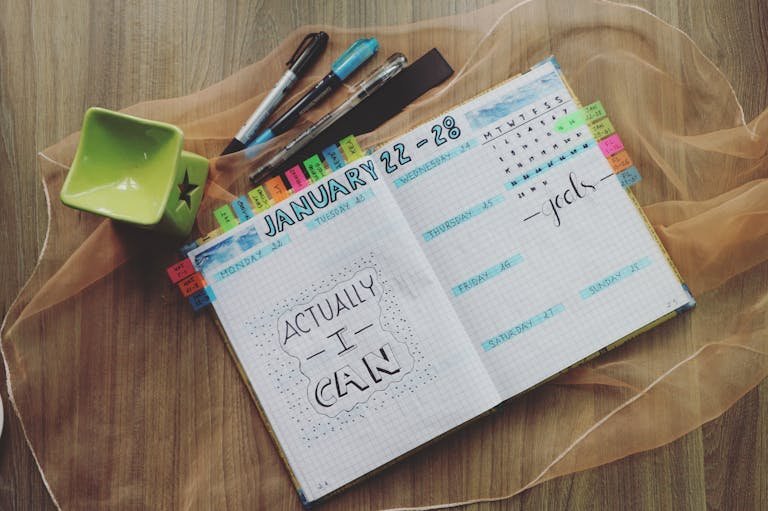 Open planner with motivational quote and colorful tabs on wooden desk.